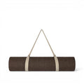 Tapis de yoga Baabuk en laine brown , enroulé et muni d'une sangle de transport en coton beige, sur fond blanc.