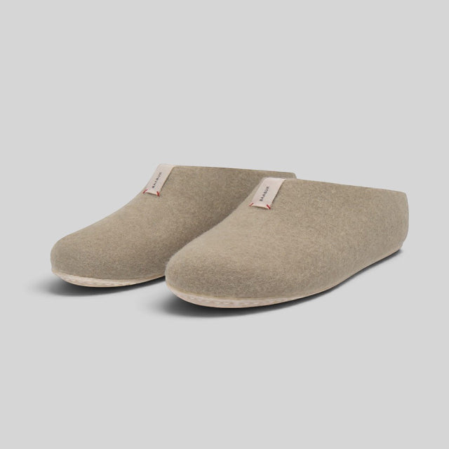 A pair of taupe felt slip-on slippers with small fabric brand tags, displayed on a neutral light gray background.