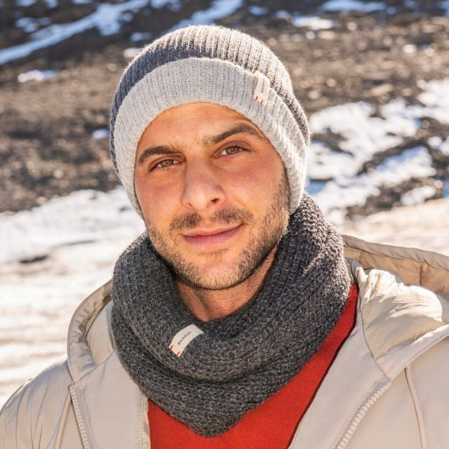 Man wearing a Baabuk dark grey baby alpaca infinity scarf and matching ribbed beanie in a snowy outdoor setting.