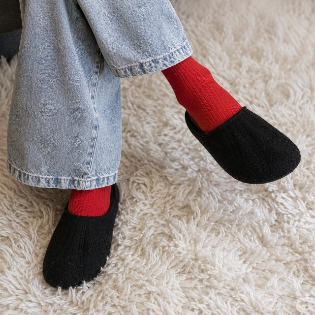 Baabuk Alpina black wool slip-on sandals worn with red socks and blue jeans on a white rug