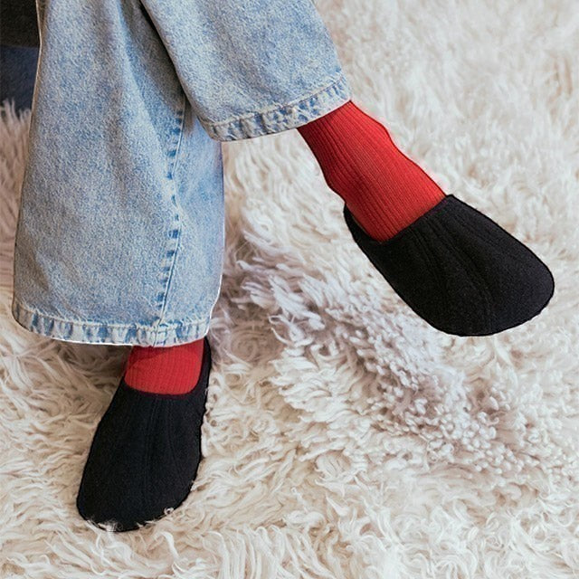 Baabuk Alpina black wool slip-on sandals worn with red socks and light wash jeans on a white shaggy rug
