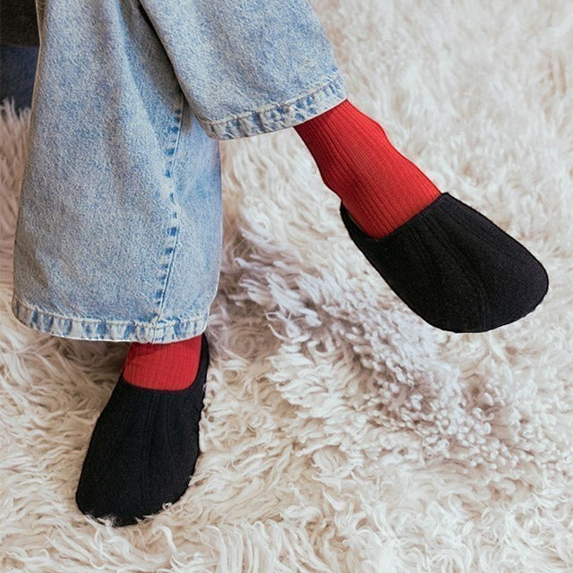 Baabuk Alpina black wool slip-on sandals worn with red socks and blue jeans on a white shaggy rug