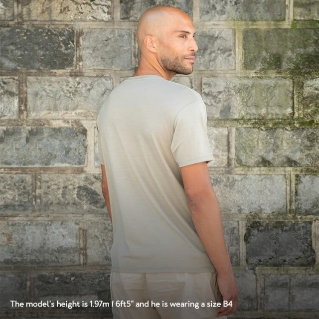 Model wearing a khaki Baabuk 10 Year Anniversary merino wool T-shirt against a stone wall background.