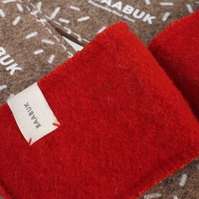 Baabuk Baabulette wool slide sandals in Swiss red with a branded fabric label, showing textured wool construction.
