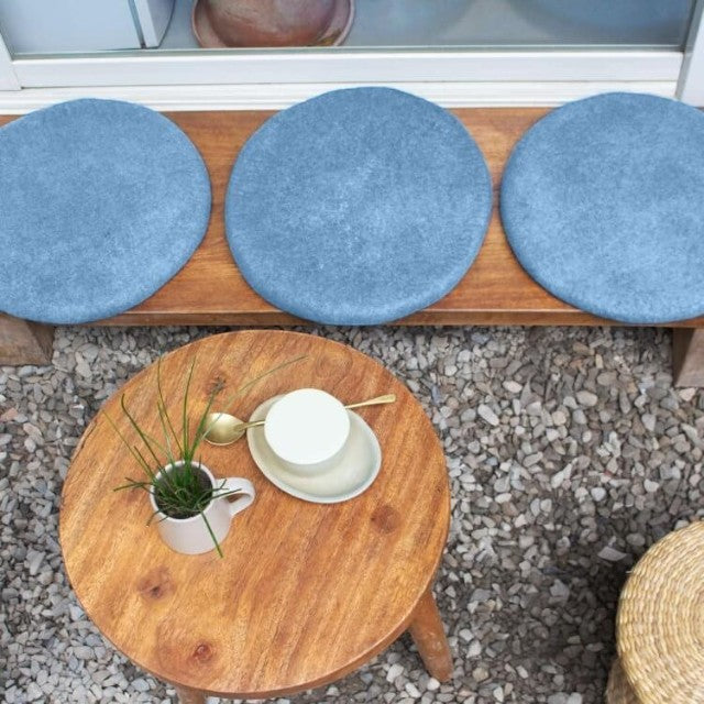 Baabuk handmade blue wool sitting mats on a wooden bench with a small table and coffee setting outdoors