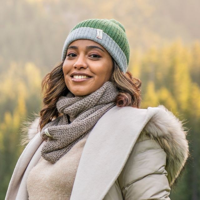 Woman wearing a Baabuk brown baby alpaca infinity scarf and green beanie in a natural outdoor setting.