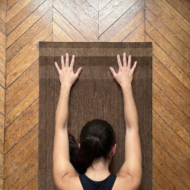 Baabuk brown felted wool yoga mat with cotton stitching, shown from above with a person in a child's pose.