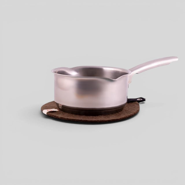 Baabuk brown felted wool trivet hot plate with a leather strap, protecting a surface under a stainless steel saucepan.
