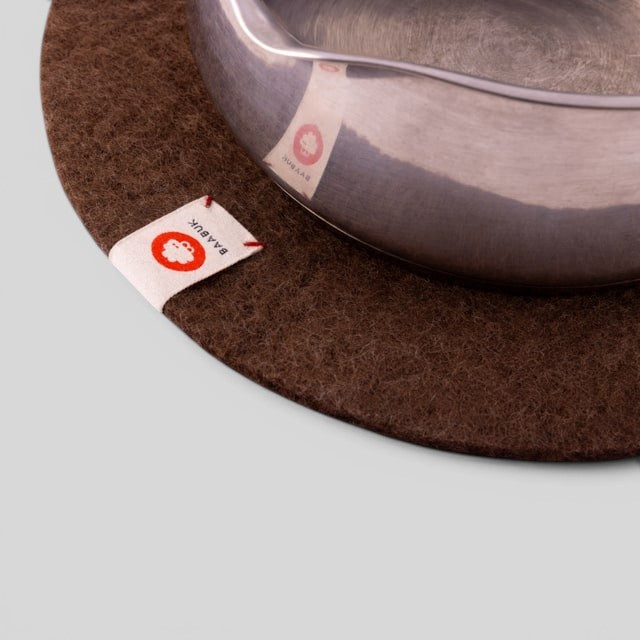 Baabuk brown felted wool trivet hot plate with a small leather brand label under a stainless steel pot
