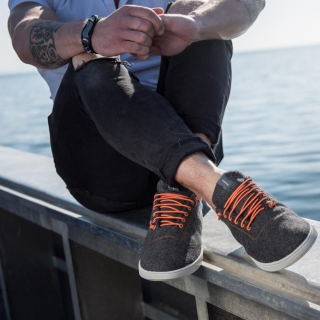 Baabuk Classic Wooler sneakers in grey wool with bright orange laces worn by a man sitting by the ocean