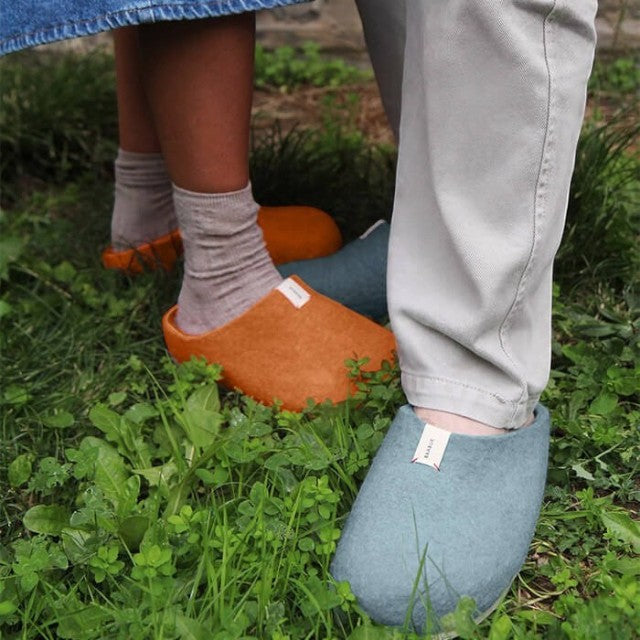 Baabuk Corkybuk slippers in light blue and orange felted wool worn outdoors on grass by two people