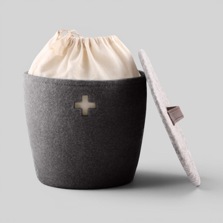 Baabuk dark grey felted wool basket with a Swiss cross cutout, leather strap lid, and internal fabric liner.