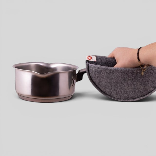 Hand holding a dark grey Baabuk felted wool potholder next to a stainless steel saucepan