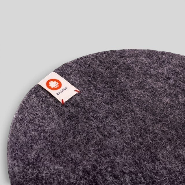 Baabuk dark grey felted wool trivet hot plate with a small branded fabric tag for kitchen surface protection.