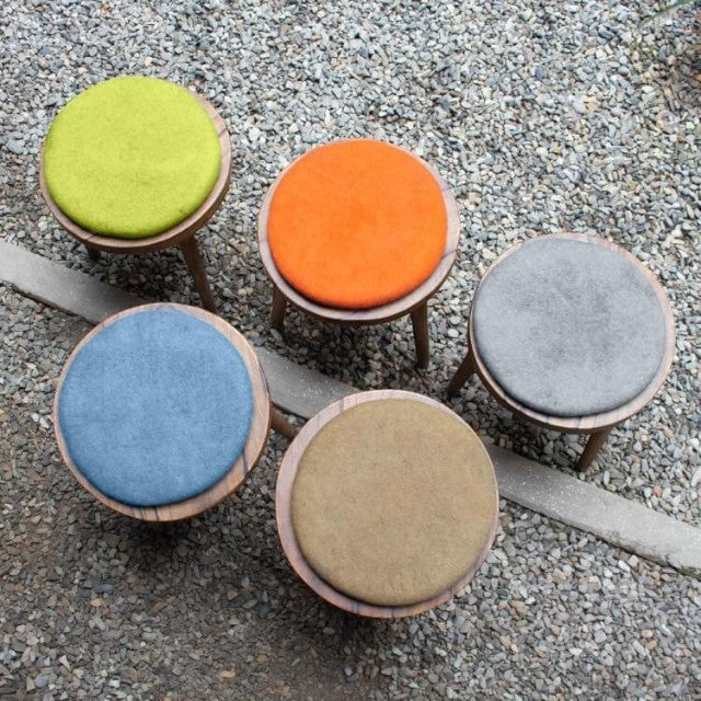Baabuk handmade wool sitting mats in various colors on wooden stools, crafted from natural New Zealand wool.