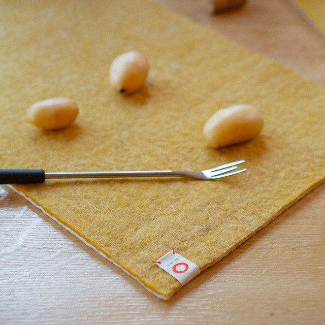 Baabuk honey yellow felted wool table mat with a small fork and potatoes on a wooden surface.