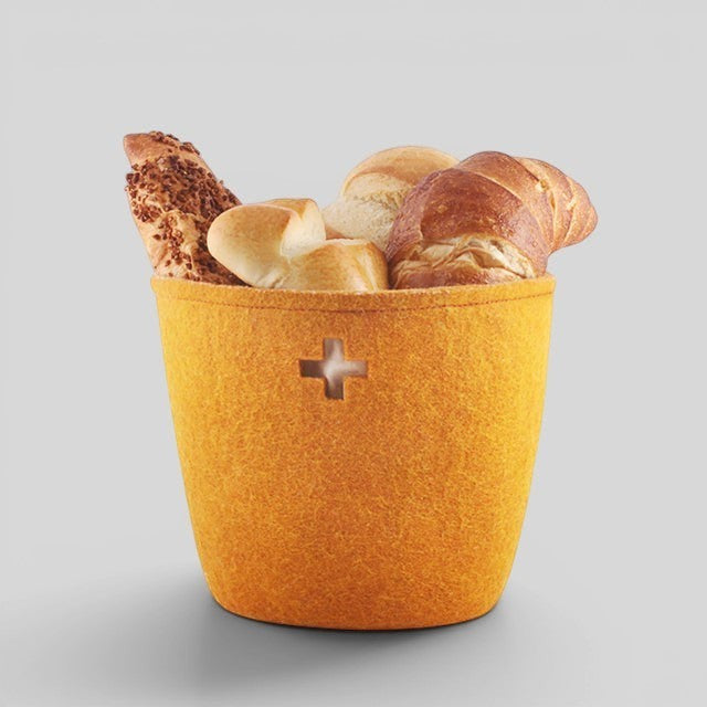 Baabuk honey felted wool basket with Swiss cross cutout, filled with assorted bread rolls on a grey background.