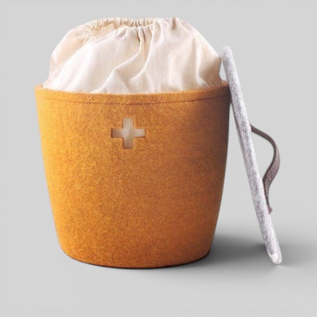 Baabuk honey yellow felted wool basket with a Swiss cross cutout, fabric liner, and a grey lid with leather handle.
