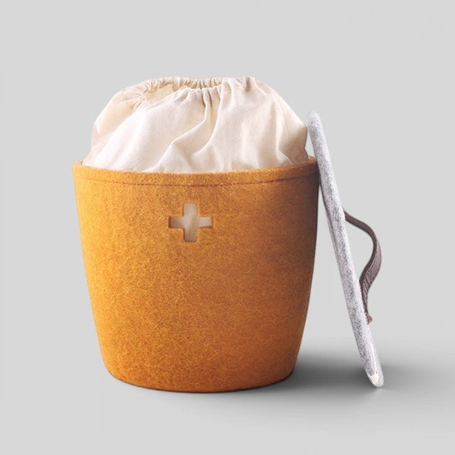 Baabuk small honey felted wool basket with Swiss cross cutout, cream fabric liner, and grey lid with leather strap.