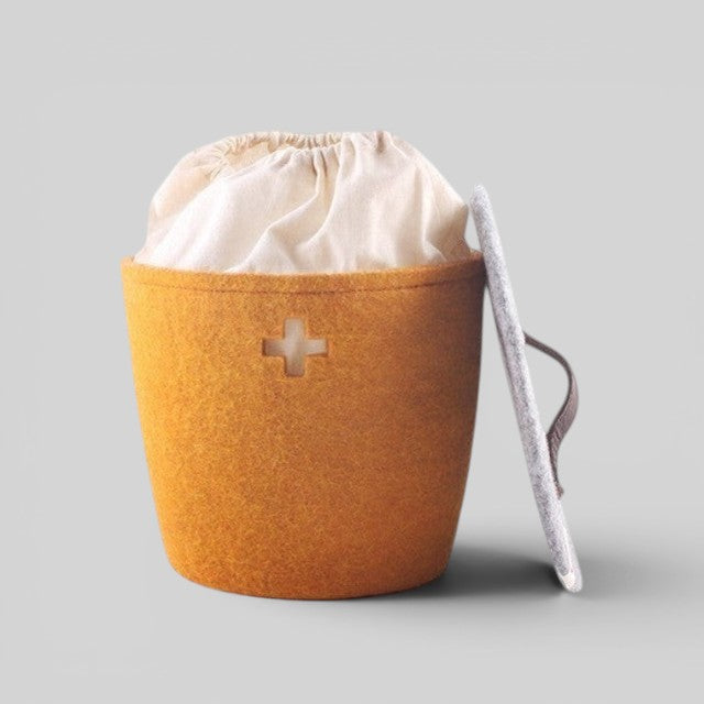 Baabuk honey yellow felted wool basket with Swiss cross cutout, fabric liner, and grey lid with leather handle.