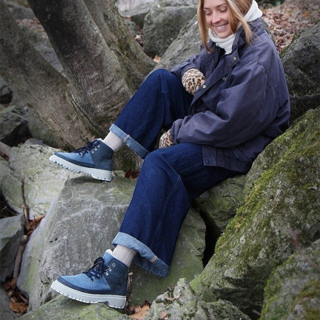 Baabuk Ice Wooler Blue Raisa wool boots with nubuck details worn by a woman sitting on rocks outdoors