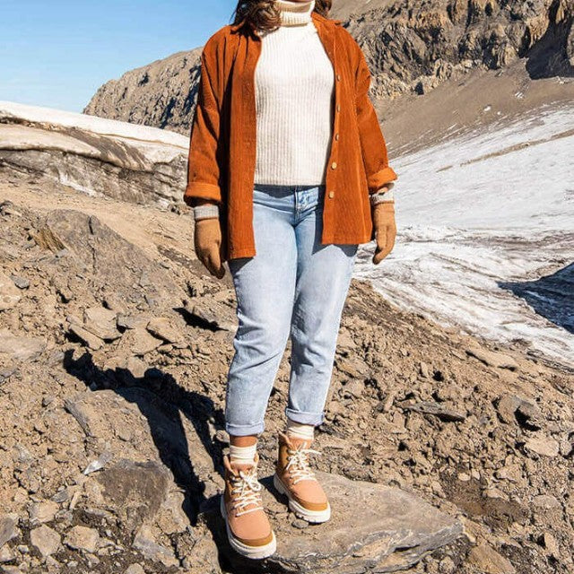 Baabuk Ice Wooler boots in Sand Rose worn by a person standing on a rocky mountain trail with snow in the background
