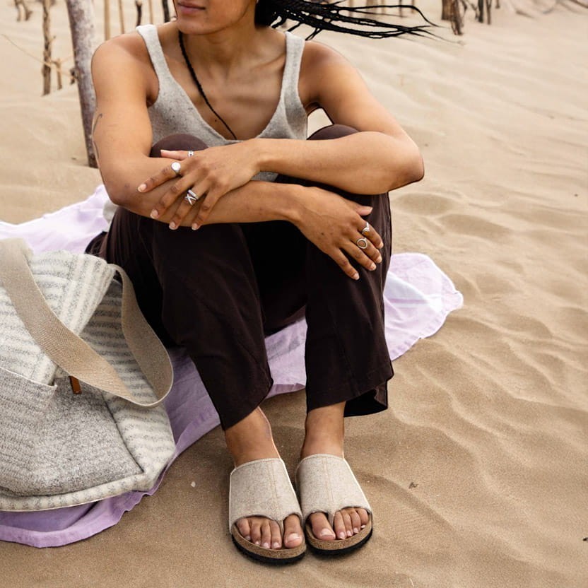 Baabuk Izard sandal with beige Pyrenean wool upper and cork footbed worn by a person sitting on a sandy beach