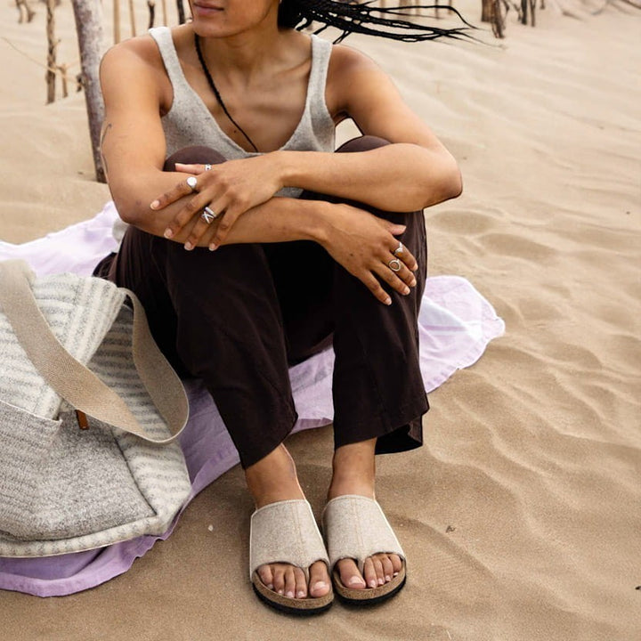 Baabuk Izard sandal with beige Pyrenean wool upper and cork footbed worn by a person sitting on a sandy beach