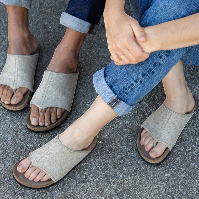 Baabuk Izard sandals featuring beige Pyrenean wool uppers and cork footbeds worn by two people on a grey surface.