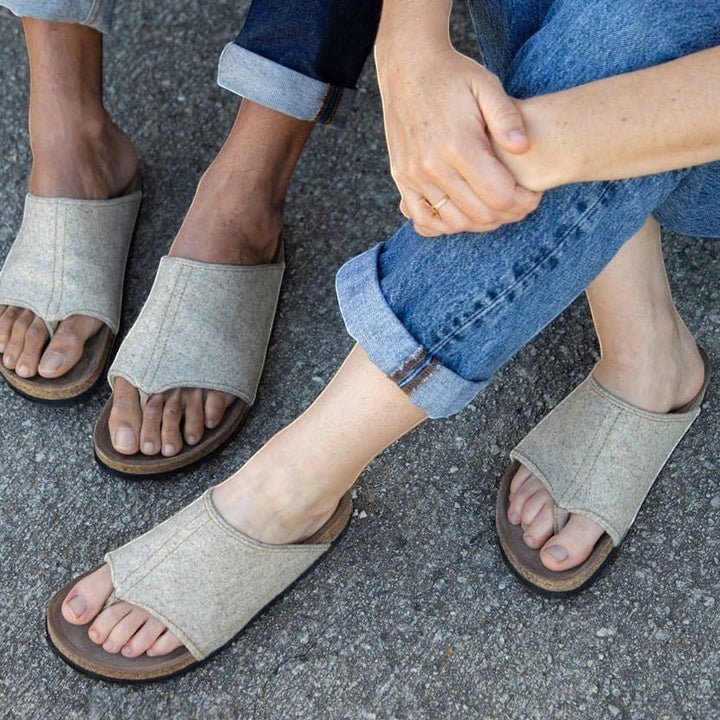 Baabuk Izard sandals featuring beige Pyrenean wool uppers and cork footbeds worn by two people on a grey surface.