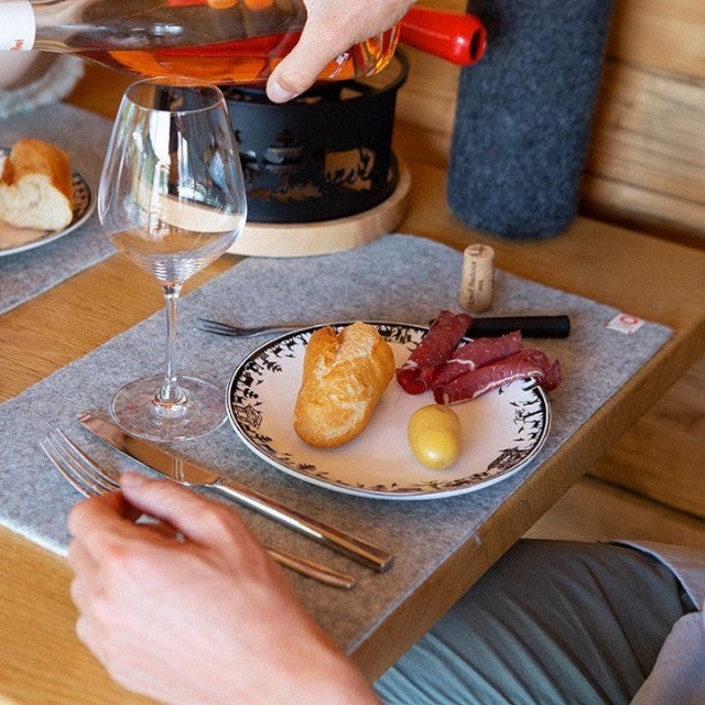 Baabuk khaki felted wool table mat on a wooden dining table with a plate of bread and wine glass