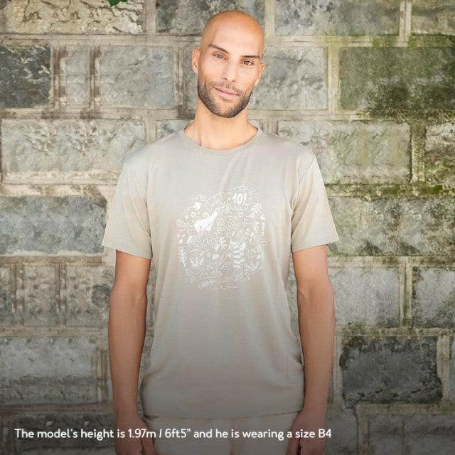Baabuk khaki merino wool t-shirt with 10th anniversary graphic, worn by a model against a stone wall background.