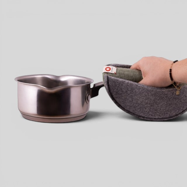 Baabuk khaki felted wool potholder held by a hand, gripping a stainless steel saucepan against a grey background.
