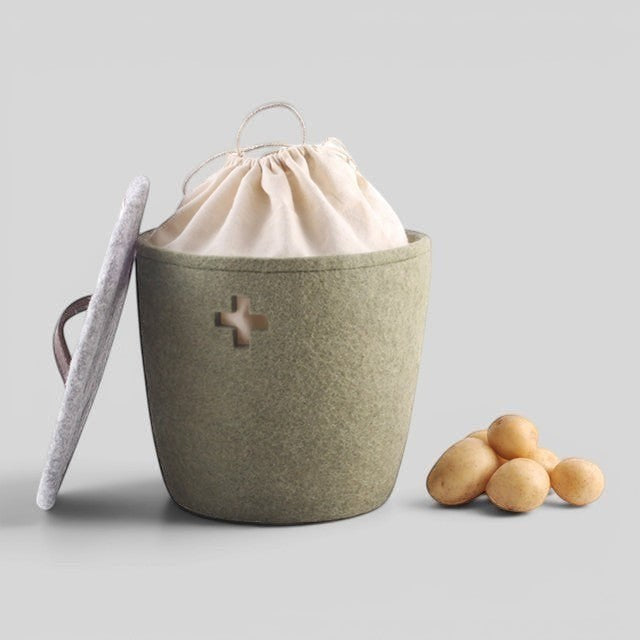 Baabuk small khaki felted wool storage basket with Swiss cross detail, fabric liner, and lid, next to potatoes.