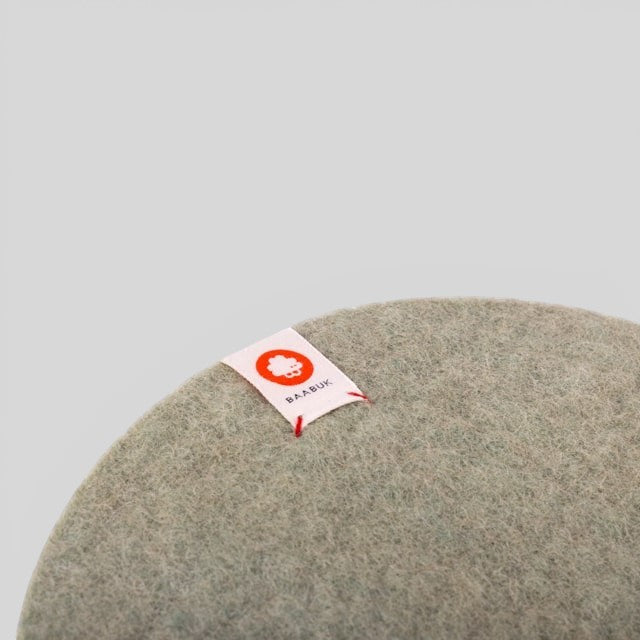 Baabuk khaki felted wool trivet hot plate with a small branded fabric tag, perfect for heat-resistant table decor.