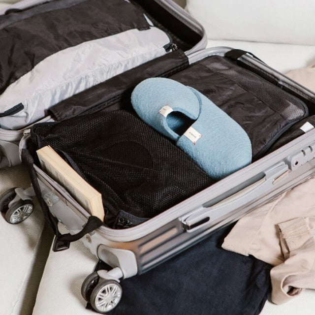 Baabuk light blue wool Kanga slippers packed inside a travel suitcase with clothing and a book.