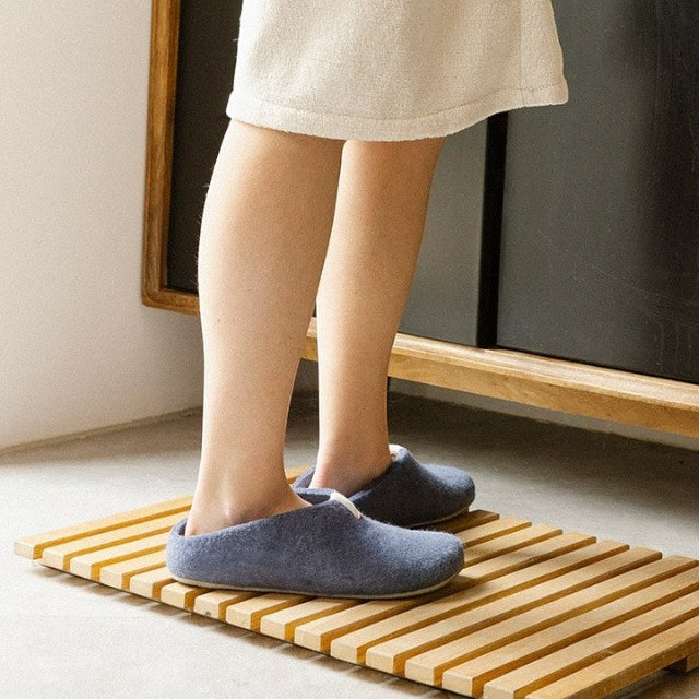 Baabuk Mel purple wool slippers with natural crepe rubber soles worn on a wooden bath mat