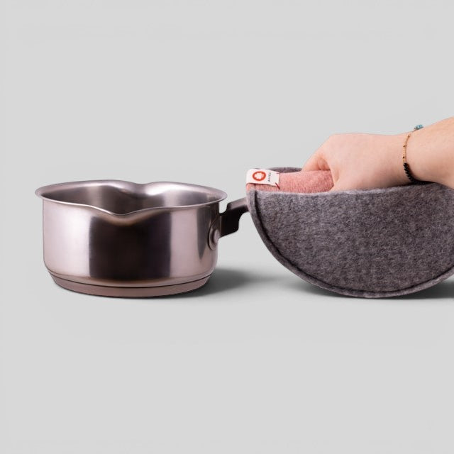 Hand using a pink Baabuk felted wool potholder to grip a stainless steel saucepan handle.
