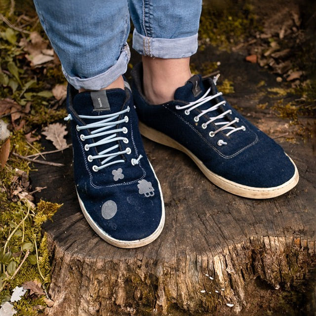 Baabuk repair kit featuring adhesive patches and elastic laces applied to navy blue wool sneakers on a tree stump.
