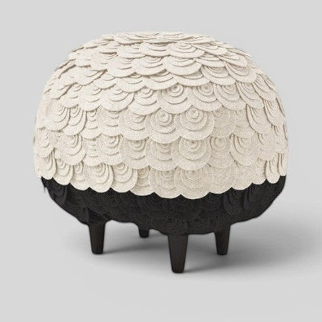 Baabuk Sheep Stool featuring cream-colored wool layers over a black felt body with four sturdy wooden legs.