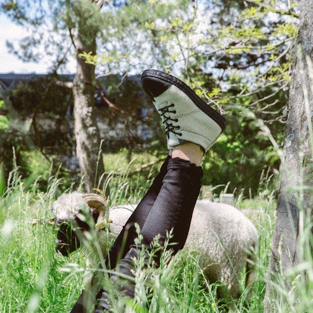 Baabuk Sky Wooler Blacknose SW sneakers in light grey wool with black rubber soles worn in a grassy field with a sheep
