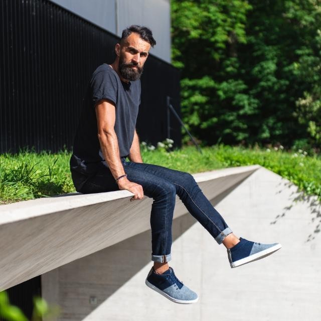 Baabuk Sky Wooler jeans sneakers in blue wool worn by a man sitting on a concrete ledge outdoors