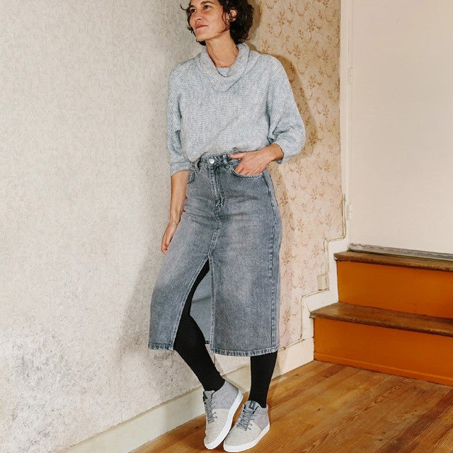 Baabuk Sky Wooler middle grey sneakers worn by a woman in a grey sweater and denim skirt in a home interior.