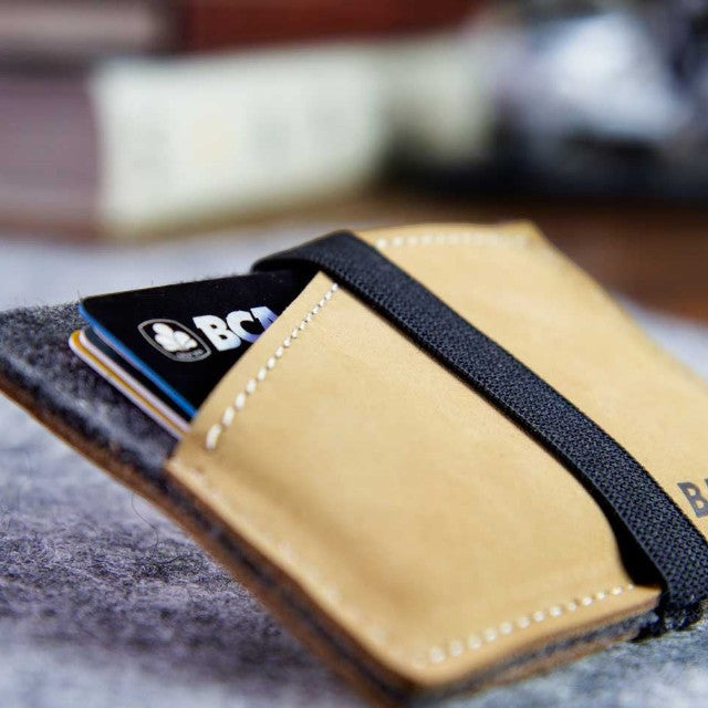 Baabuk slim wallet made of natural wool and tan leather with a secure black elastic strap holding credit cards.
