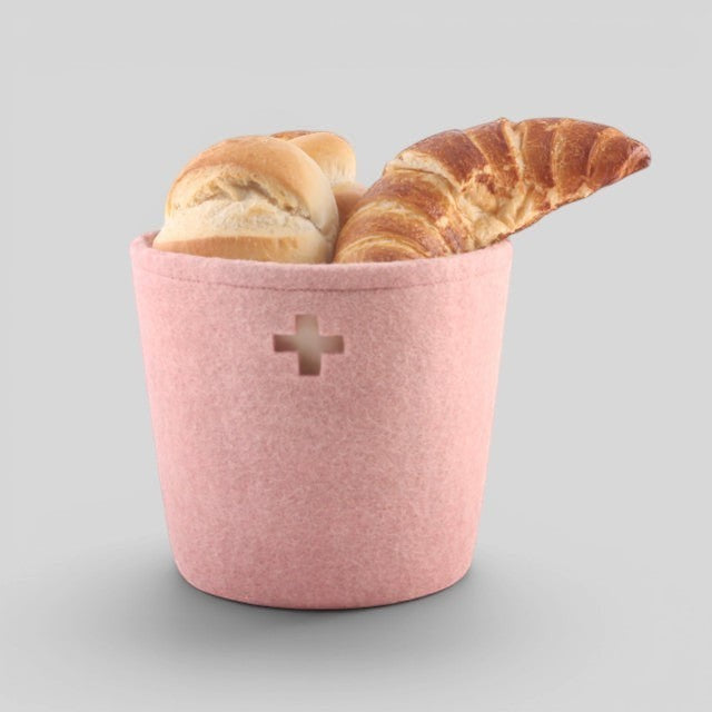 Baabuk small pink felted wool basket with a Swiss cross cutout, holding fresh bread and a croissant.