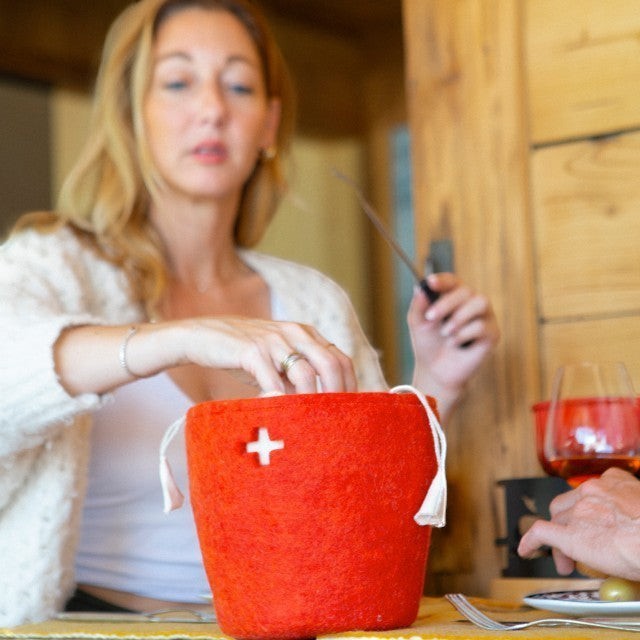 Baabuk small red felted wool basket with Swiss cross detail on a dining table during a fondue meal.