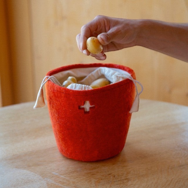 Baabuk small Swiss red felted wool basket with a cross cutout, holding potatoes on a wooden table.