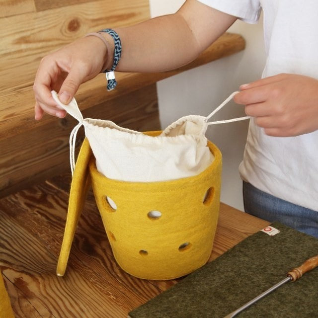 Baabuk small yellow felted wool basket with Swiss cheese design and white fabric drawstring liner on wooden table.