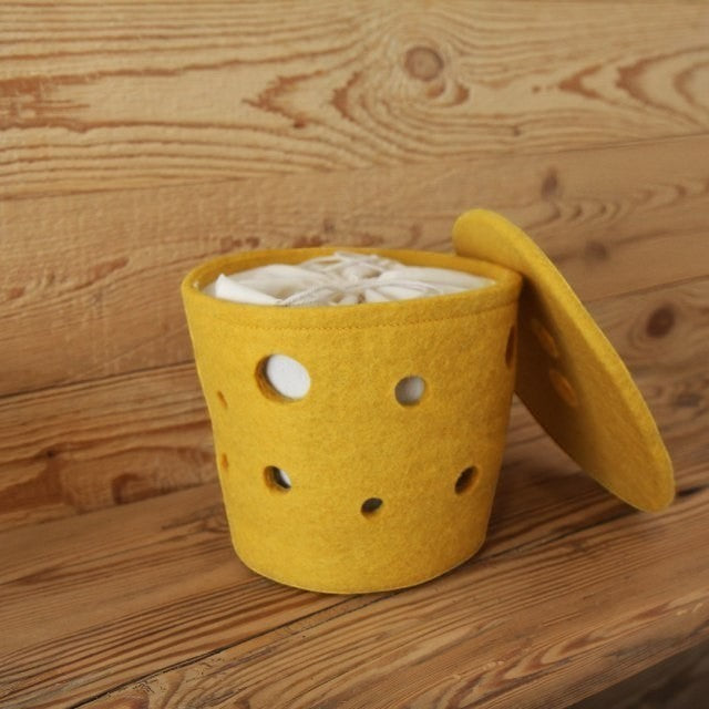Baabuk small yellow felted wool basket with Swiss cheese hole design on a wooden surface.