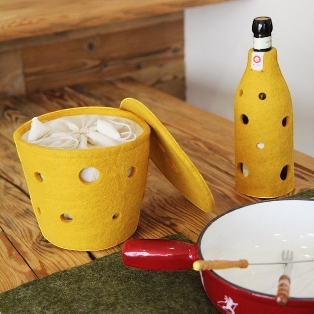Baabuk yellow felted wool bottle cover and matching container with Swiss cheese hole design on a wooden table.